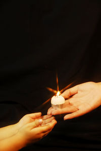 Close-up of hand holding illuminated candle against black background