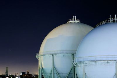 Low angle view of gas tanks in industry against sky at night