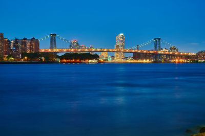 Illuminated buildings by sea against blue sky