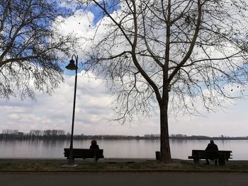 Silhouette people sitting on bench by lake against sky