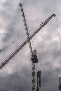 Low angle view of cranes at construction site against sky