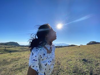 Woman standing on field against blue sky on sunny day