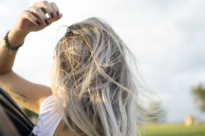 Close-up of young woman peeking from car against sky