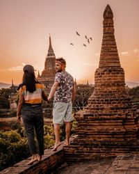 Rear view of couple standing at temple against sky during sunset