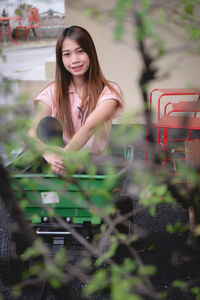 Portrait of young woman sitting in wheelbarrow against wall