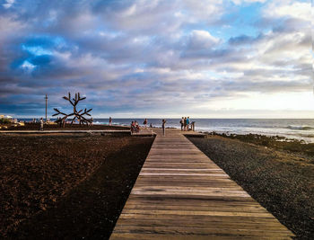 Wooden boardwalk at beach against cloudy sky
