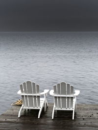 Empty chairs at beach against sky