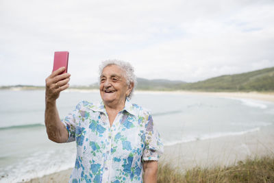 Happy senior woman taking selfie on the beach