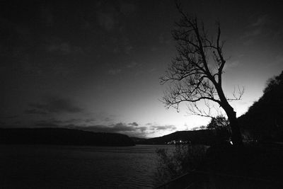 Silhouette bare tree by lake against sky