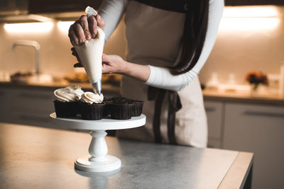 Woman decorate chocolate muffins with whipped cream cheese in kitchen table closeup. 