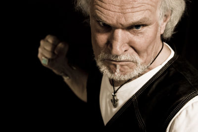 Portrait of angry senior man with clenching fist against black background
