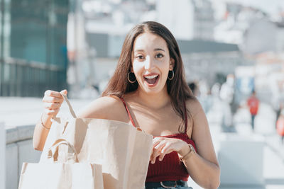Portrait of young woman holding shopping bags while standing outdoors