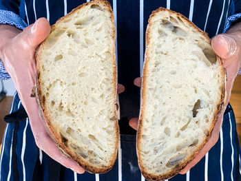 Man in stripped blue apron holding freshly baked sourdough bread.traditional french loaf.cut in half