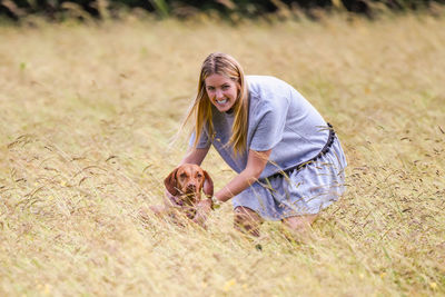 Portrait of happy woman with dog standing amidst field