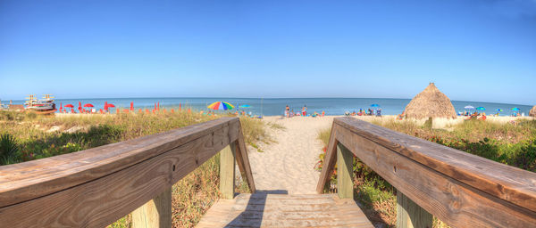 Boardwalk leading towards sea against clear blue sky