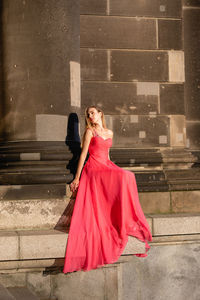 Full length of woman wearing red evening gown sitting on steps
