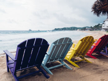 Colorful deck chairs on shore at beach against sky