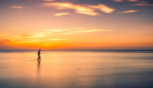 Silhouette man surfing on sea against sky during sunset