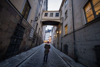 Rear view of woman walking on footpath amidst buildings in city