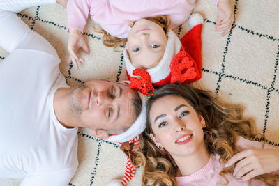 Family in santa hats with their daughter, in light, cozy clothes, lying