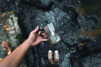 Cropped hand of man holding container while standing by flowing stream