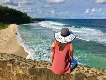 Rear view of woman sitting retaining wall against beach