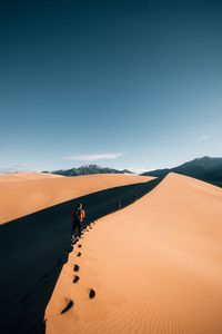 Rear view of people walking on sand dune at desert against blue sky