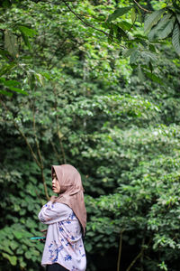 Rear view of woman standing amidst plants in forest