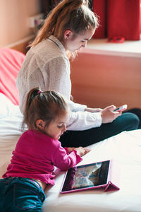 Sisters using technologies on bed at home