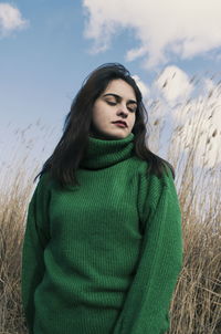 Portrait of beautiful young woman standing in field against sky