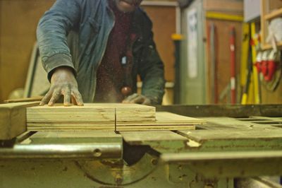 Midsection of carpenter cutting plank at workbench in workshop