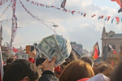 People holding paper currency in city against sky