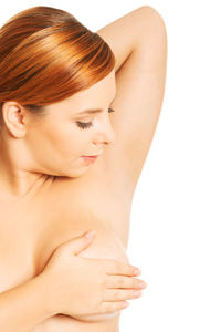 Close-up of shirtless woman covering breast against white background