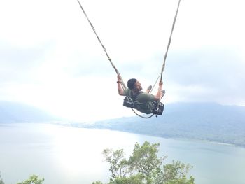 Man jumping on swing against sky