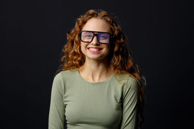 Portrait of young woman standing against black background