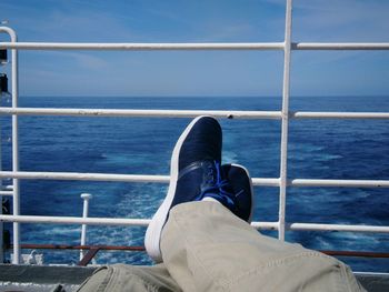 Low section of man relaxing by sea against sky