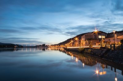 Illuminated buildings by lake against sky at night