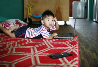 Boy using laptop while lying on bed at home