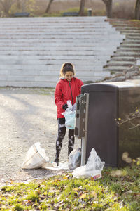 Female volunteer throwing plastic waste in garbage can against staircase