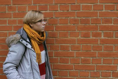Young woman wearing warm clothing while standing against red brick wall