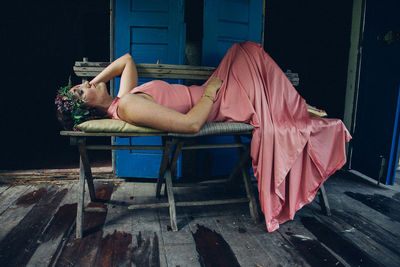 Young woman wearing peach gown while lying on bench at old house