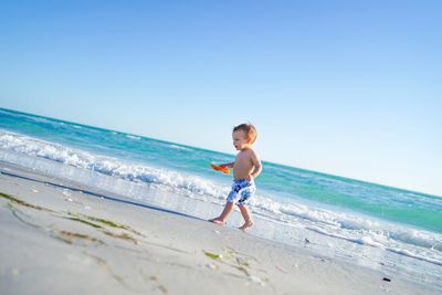 Shirtless boy walking on shore against sky