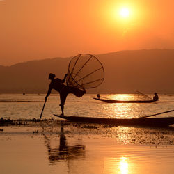 Silhouette men fishing in lake during sunset
