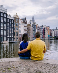 Rear view of people sitting on canal against buildings in city