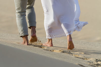 Low section of two  people walking on sand against sky