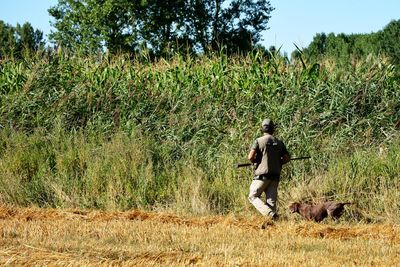 Rear view of man holding gun while standing on field