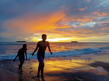 People on beach against sky during sunset