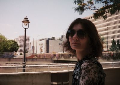 Portrait of woman wearing sunglasses in city against sky