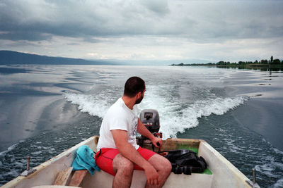 Rear view of men sitting on sea against sky