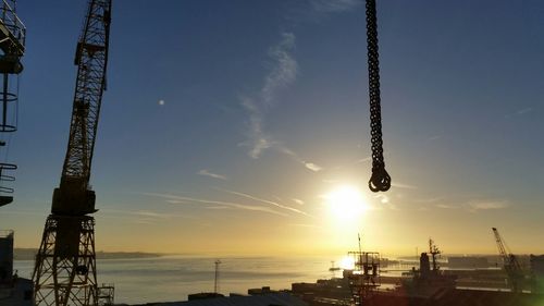 Crane at harbor against sky during sunset